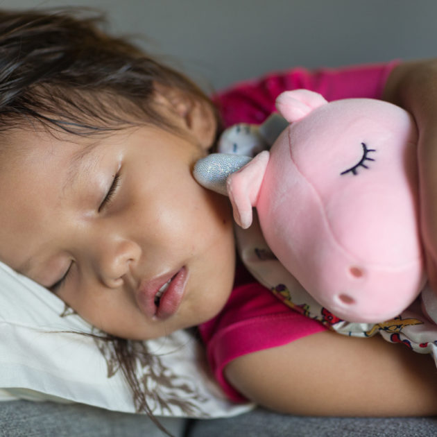 A little girl sleeping with a stuffed pig.