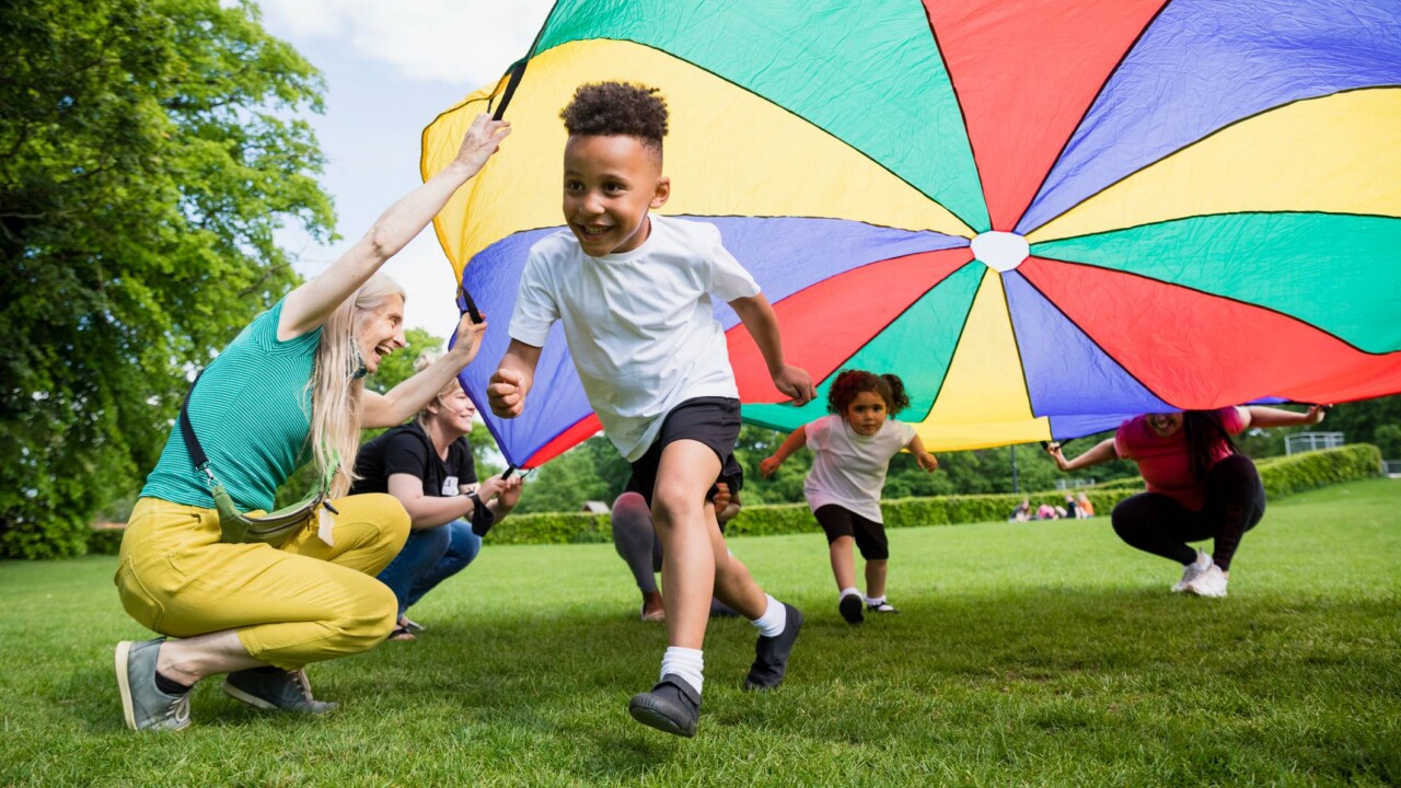 A group of children playing with a colorful parachute in a park.